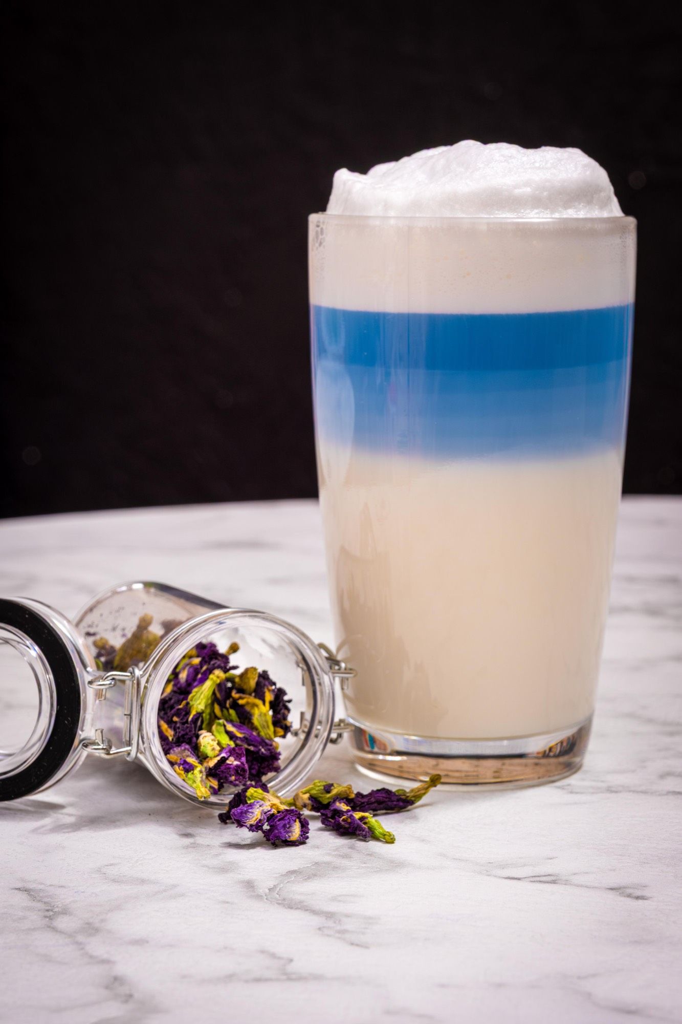 Le Butterfly Latte servi bleu, bocal de fleurs de pois papillon renversé sur le marbre