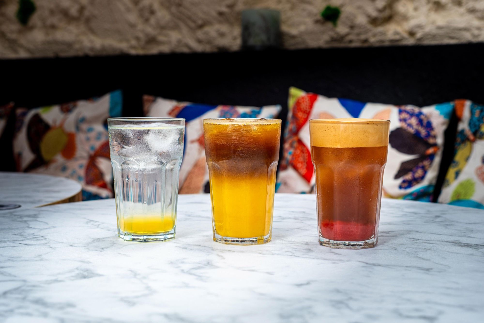 Trois boissons fraîches alignées sur le marbre devant les coussins colorés — la pause d’équipe chez PEACH