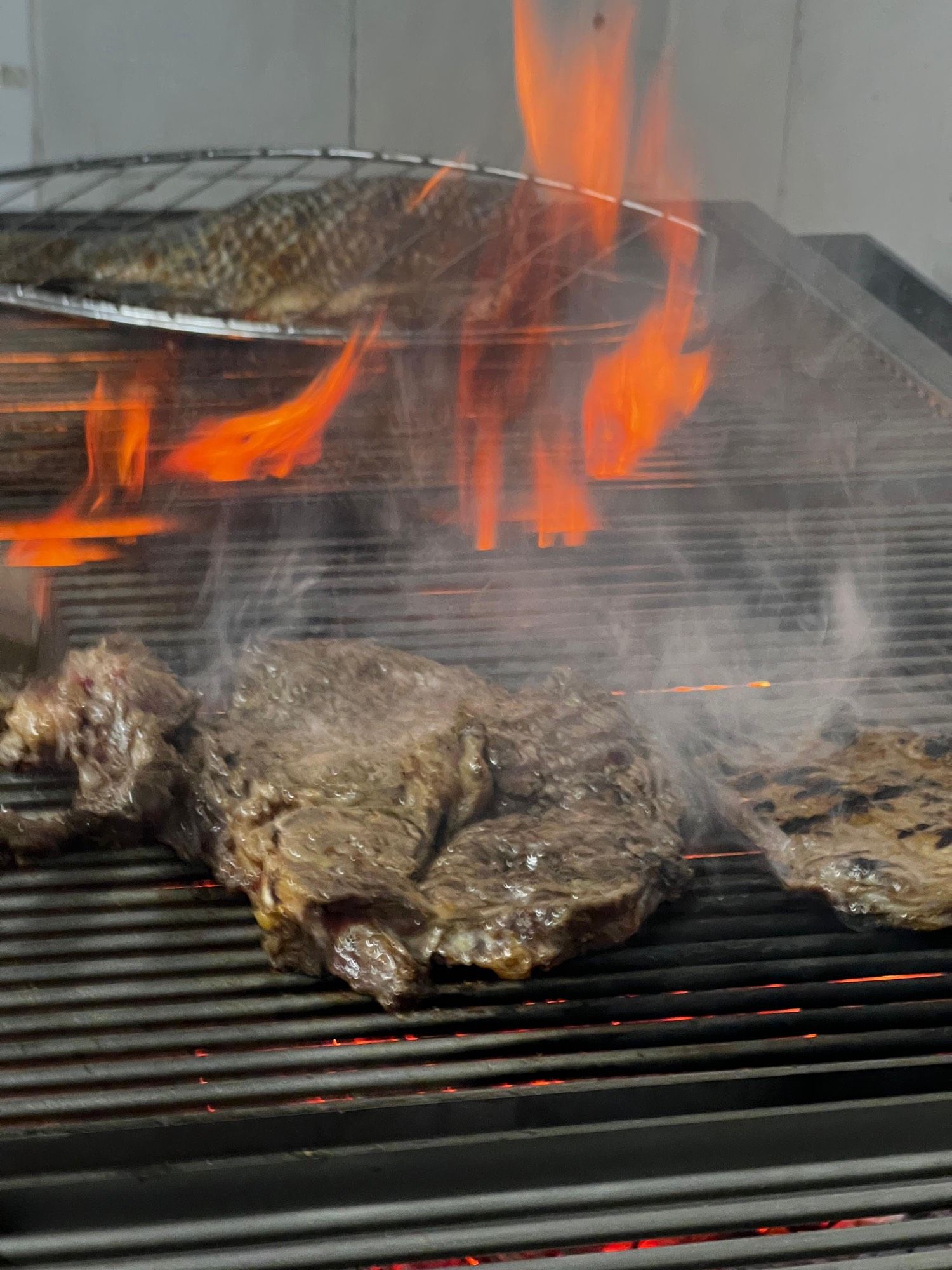 Pièce de bœuf grillée au-dessus des braises rougeoyantes, flammes en arrière-plan