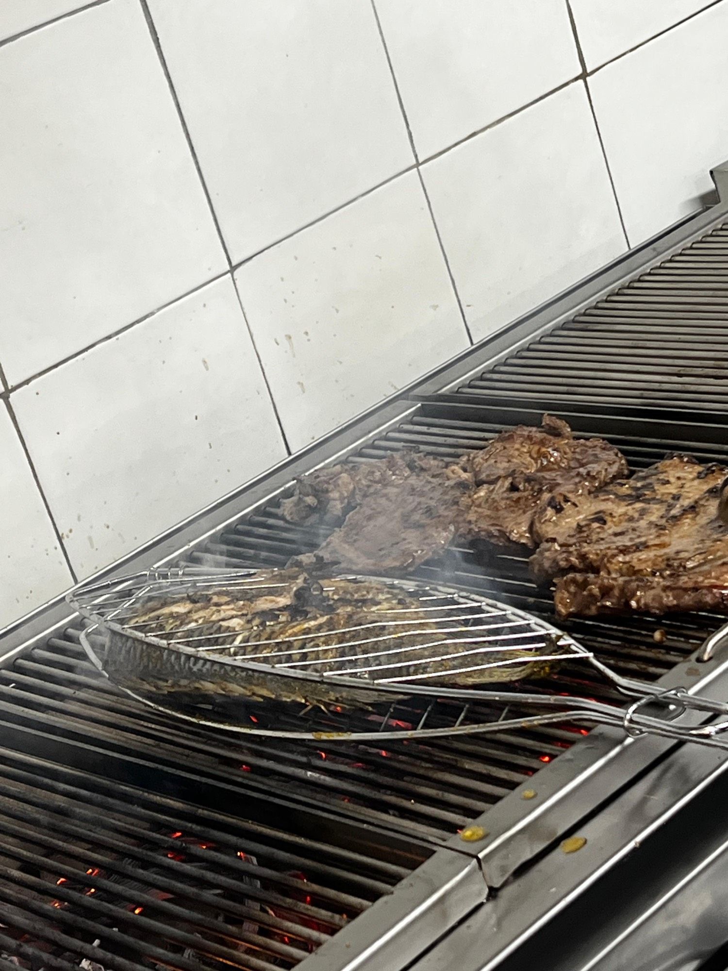 Pièces de bœuf et tilapia entier en cuisson sur la braise