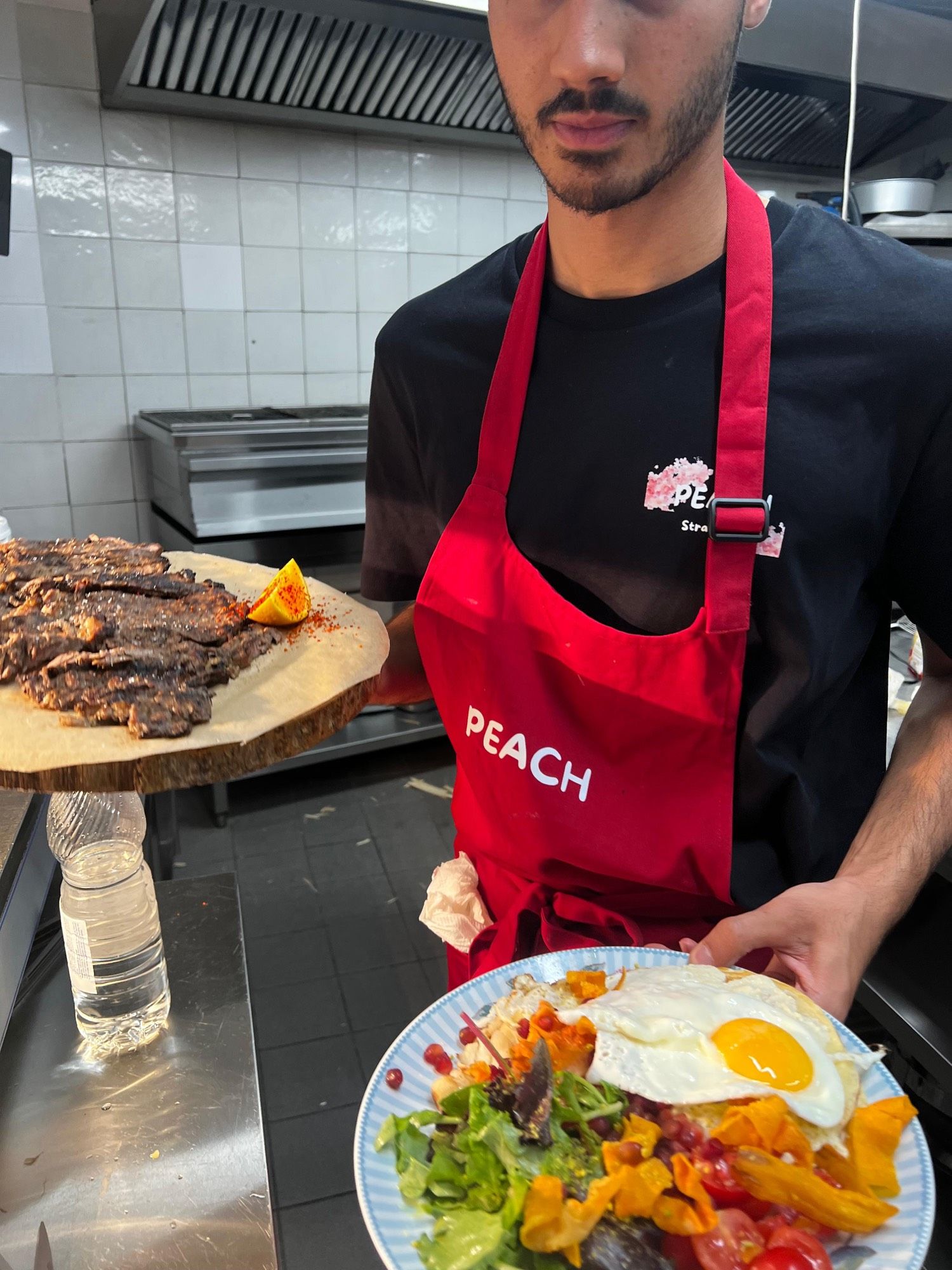 Un équipier PEACH apporte en salle une planche de bœuf grillé et une assiette de salade, un soir de service