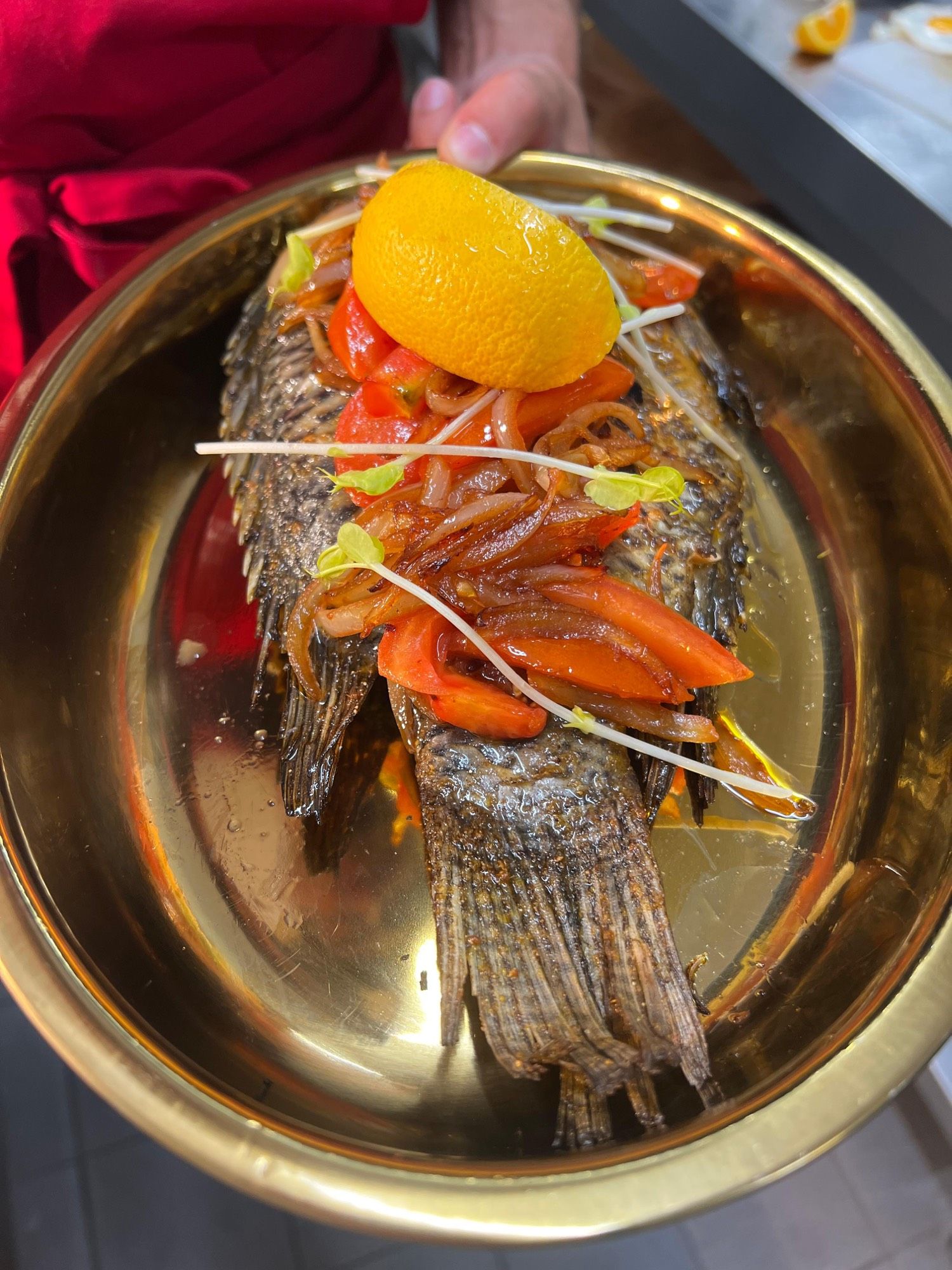 Tilapia braisé entier servi dans un plat doré, tomates et oignons fondants