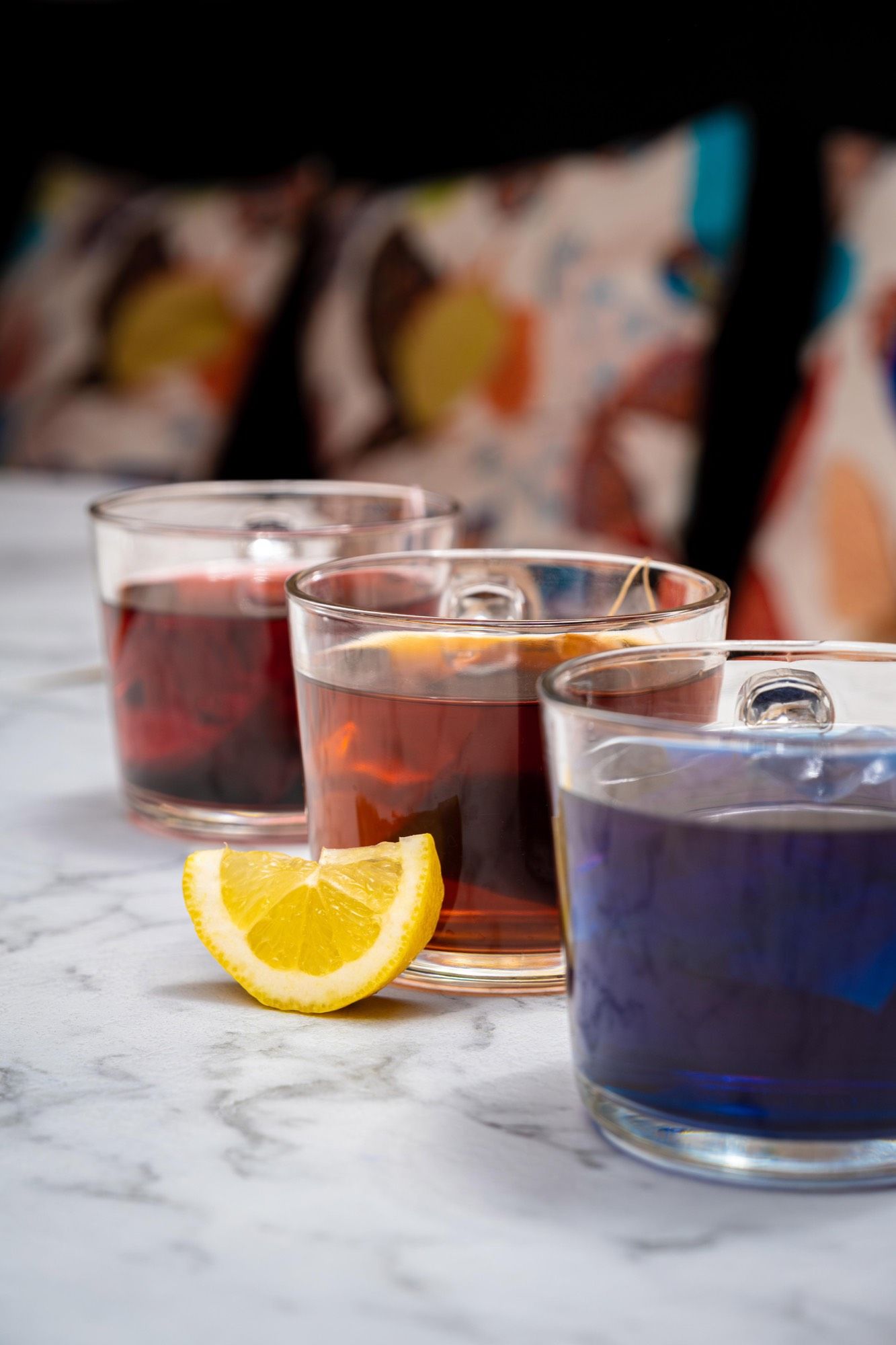 Trois infusions colorées — pourpre, ambre, bleu — posées sur la table, prêtes à être servies